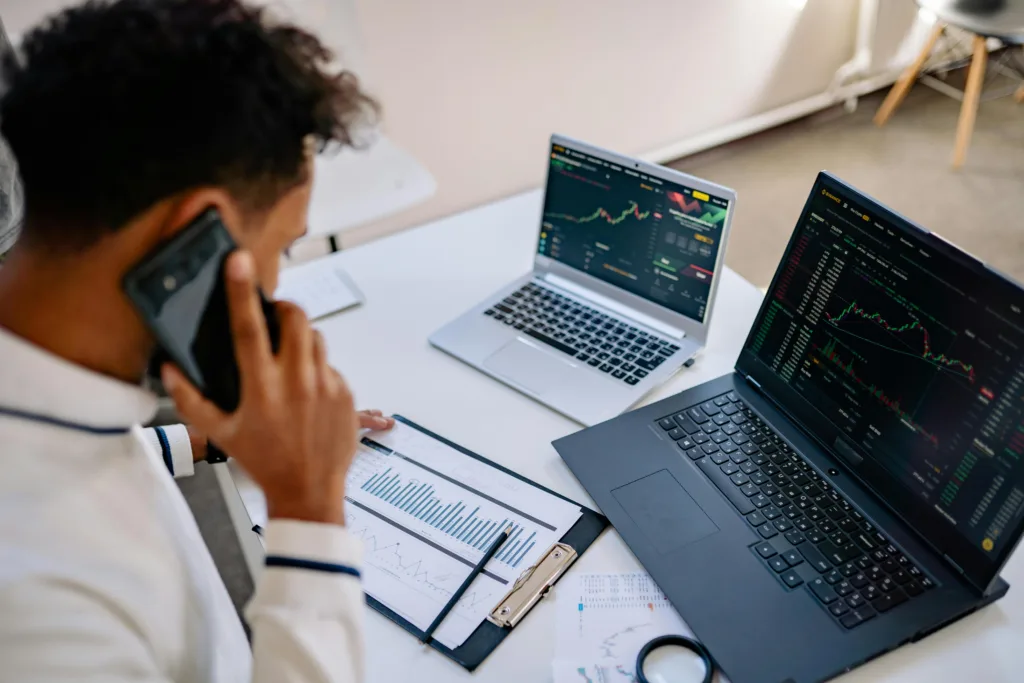 empresario hablando por teléfono mientras gestiona clientes en dos portátiles con datos de ventas.